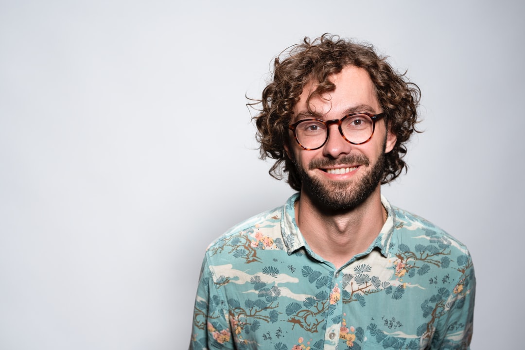 A profile picture of a man, early 30s and smiling, against a soft gray background.