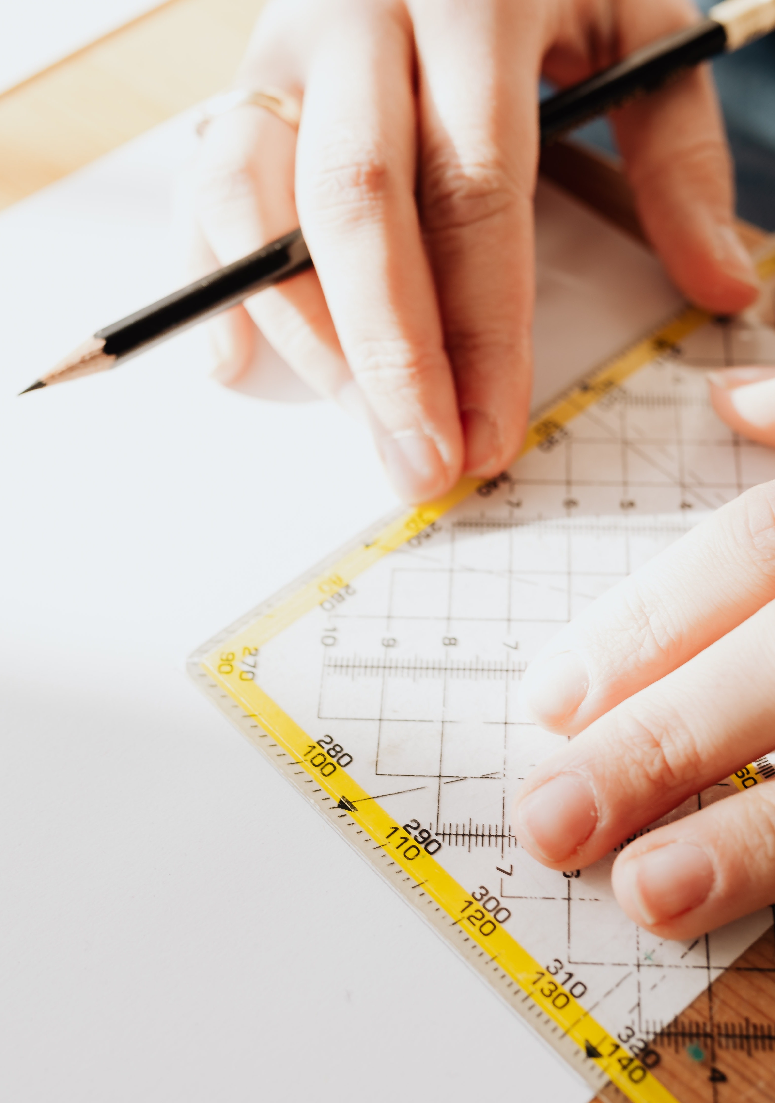 Two hands, one holding a pencil and the other holding a right-angled ruler, preparing to draw a line.